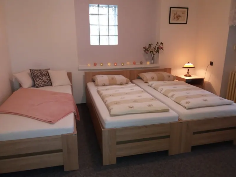 Třílůžkový pokoj s postelemi u okna a křeslem